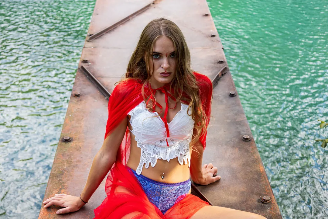Seduta su un pontile sopra l'acqua turchese, con il mantello rosso.